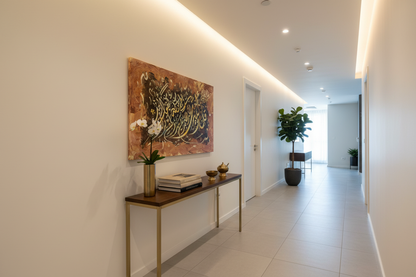 Islamic calligraphy gold and white canvas displayed in a modern hallway, no frame